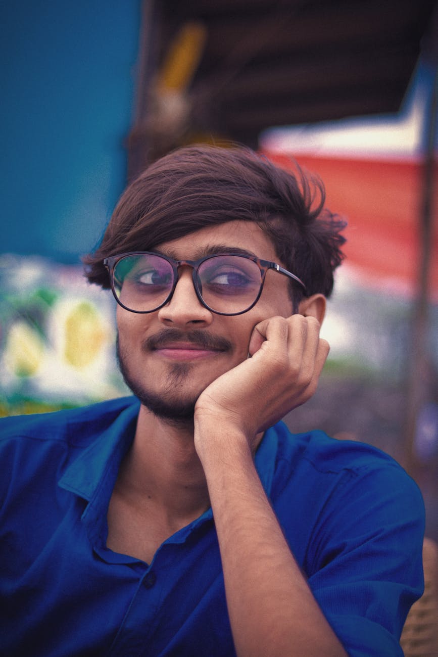 Portrait of a young man with eyeglasses smiling playfully outdoors.